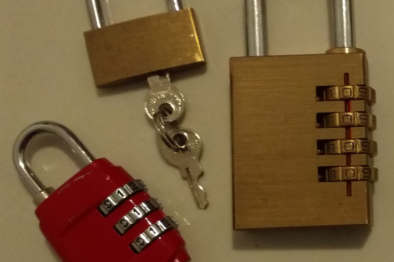 Three padlocks on a plain surface, two with number dials and one with a pair of keys