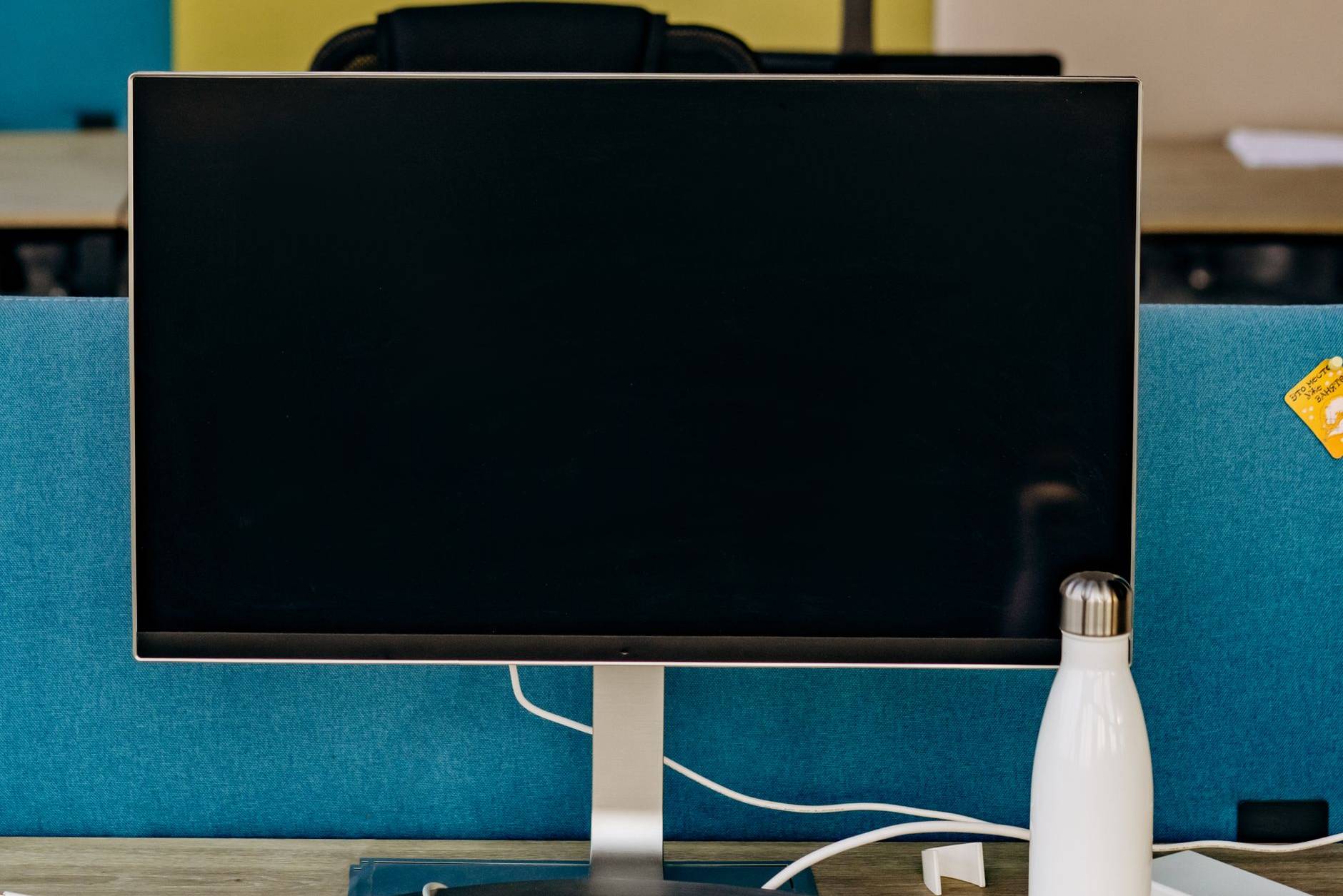 Office desktop monitor with a dark screen on a desk in an open-plan office